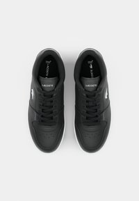 Adidași negri din piele cu vârf perforat, accente albe și șireturi. Prezintă logo-ul Lacoste pe laterale și branțuri marcate. Design clasic cu talpă joasă.