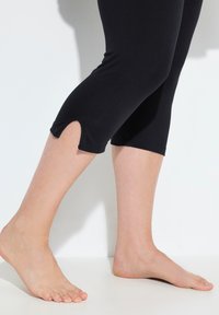 Leggings capri negros con un diseño ajustado, que presentan una abertura lateral en el dobladillo para mayor libertad de movimiento. Tejido suave y elástico.