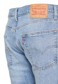 Ljust blå denimjeans med en urtvättad finish, prydda med en läderlogotyp, bakfickor och klassiska sömdetaljer i ett svängt mönster.