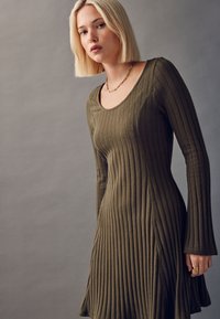 Olivgrünes, geripptes Kleid mit langen Ärmeln und einem abgerundeten Ausschnitt, ausgestattet mit einem taillierten Oberteil, das am Saum ausgestellt ist, aus strukturiertem Stoff.