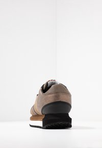 Brown sneaker featuring a mesh upper, leather accents, a stacked sole with black rubber tread, and a cushioned collar. Rear view.