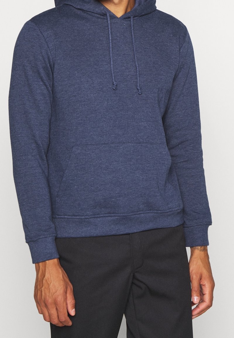 Námořnická modrá mikina s kapucí, se přední kapsou typu "kangaroo", žebrovanými manžetami a lemem, vyrobená z texturované tkaniny. Těsně obepíná trup.