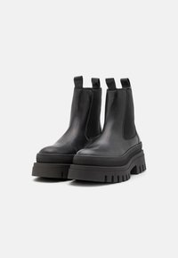 Black leather Chelsea boots with elastic side panels, pull tabs, chunky rubber soles, textured detailing, and a sturdy, rounded design.