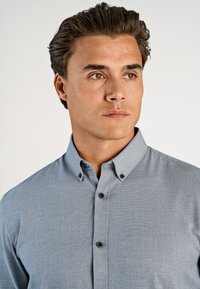 Lichtblauwe overhemdbloes met een kraag, gemaakt van een gestructureerde stof, met twee knopen op de kraag en een getailleerd ontwerp.