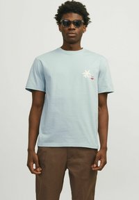 Camiseta de algodón azul claro con mangas cortas, con un gráfico de palma y un diseño de texto en blanco y rojo en el área del pecho izquierdo.