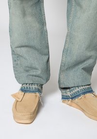 Beiga mockasiner i mocka med rå kant, i kombination med ljusblå slitna jeans med fransade fållar och kontrasterande manschetter.