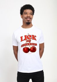 Hvid bomulds t-shirt med fed rød tekst, der står "LICK my CHERRIES", med to realistiske røde kirsebær trykt nedenunder.