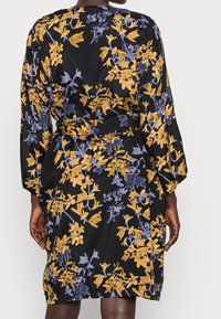 Zwarte stoffen jurk met een bloemenpatroon in geel en blauw. Lange mouwen, met een ceintuur in de taille en een lengte tot op de knie. Soepele textuur.