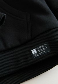 Schwarzer Sweatshirt mit gerippten Bündchen und Saum, mit einem Etikett, das Markeninformationen und Pflegehinweise zeigt. Weicher Stoff.