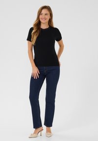 Haut noir à manches courtes avec un col en dentelle texturée, associé à un jean slim bleu marine et à des mules beiges à talons. Design simple et ajusté.