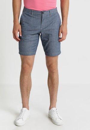 Niebieskie szorty dżinsowe z zapięciem na guzik, szlufkami na pasek i kieszeniami po bokach. Gładka tekstura i prosty krój, w połączeniu z białymi trampkami.