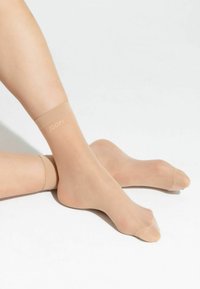 Calzini alla caviglia beige con una texture liscia, dotati di un logo JOOP! sulla parte superiore. Il materiale sembra trasparente e leggero.