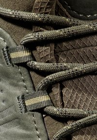 Gros plan sur une botte de randonnée verte avec un tissu texturé, des lacets tressés et des œillets renforcés présentant un détail en bande horizontale.