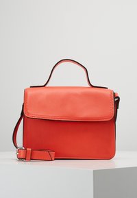 Sac à main en cuir corail avec une poignée supérieure unique, une bandoulière ajustable, un fermoir à rabat, un bord contrasté noir et une texture lisse.