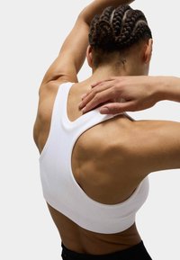 Top sportivo bianco con un design testurizzato, spalline larghe e taglio racerback, che offre una vestibilità aderente e flessibilità per l'abbigliamento sportivo.