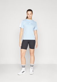 Camiseta atlética color azul claro, pantalones cortos negros, calcetines deportivos blancos con rayas negras y zapatillas blancas. Presenta el logo de Adidas en el pecho y las mangas.