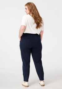Navyblauwe broek met een elastische tailleband en achterzakken, gecombineerd met een witte top met korte mouwen, met een gladde textuur en een getailleerde pasvorm.