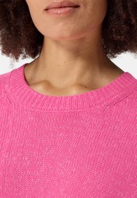 Pull en tricot fuchsia avec un col ras du cou côtelé. La texture est douce et légèrement ample, avec un léger éclat et des coutures détaillées.