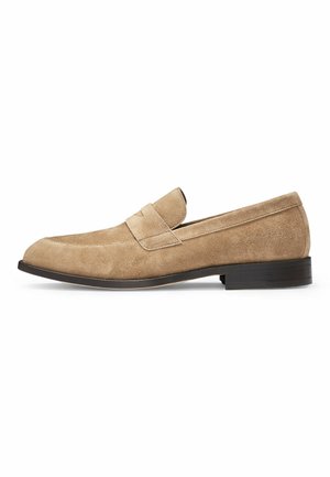 Tan suede slip-on loafer with a rounded toe, decorative strap detail, and a low black rubber heel. Smooth texture throughout.