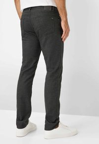 Mørkegrå slim-fit bukser lavet af tekstureret materiale, med lige snit, baglommer og en mærkevare talje, kombineret med hvide sneakers.