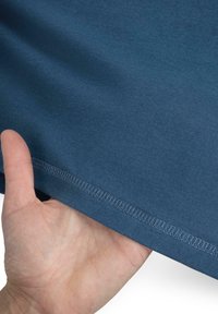 Dunkelblauer Stoff mit glatter Textur und sichtbarem Saum, der von einer Hand gehalten wird. Die helle Naht umreißt die Kante.