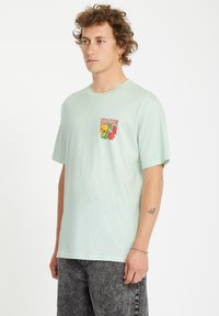 Camiseta de algodón verde menta claro con cuello redondo y un gráfico en el pecho de una flor amarilla y la palabra "YELLOW" en rojo.