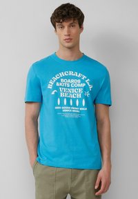 Heldere blauwe t-shirt met korte mouwen, versierd met witte grafische teksten en ontwerpen gerelateerd aan Venice Beach, gemaakt van zachte katoen.