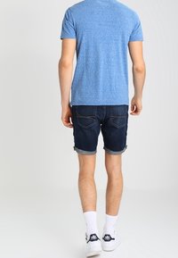 Modrý heather crew neck tričko, tmavé džíny šortky s ohrnutým lemem, bílé ponožky a bílé sportovní boty s černými akcenty.