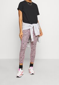 Svart kortärmad t-shirt, grå sweatshirt knuten i midjan, rosa leopardmönstrade leggings och vita sneakers med rosa detaljer.