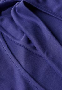 Fioletowy materiał o gładkiej teksturze, z drapowanymi fałdami i detalami szycia. Materiał wydaje się elastyczny i lekki.