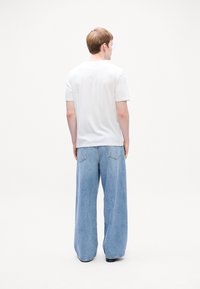 Hvit t-skjorte med kort erm kombinert med lyseblå vide jeans med baklommer, synlige sømmer og en avslappet passform.