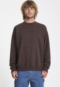 Brązowa bluza z okrągłym dekoltem, z kontrastowym czarnym logo "VOLCOM" wyszytym na klatce piersiowej. Miękka tkanina, luźny krój i ściągacze przy mankietach.