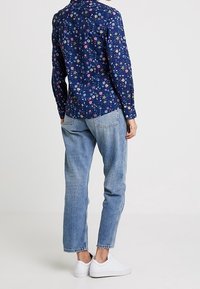 Navy floral button-up shirt with long sleeves, paired with light blue denim jeans and white sneakers, viewed from the back.