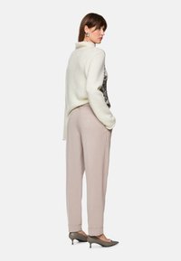 Cream sweater with a high collar and textured knit, paired with light pink tailored pants. Model wears green heels, showcasing a sleek design.