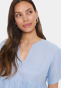Light blue blouse with short sleeves, V-neckline, textured with horizontal stripes, and a gathered waist. Features a soft, shiny fabric.