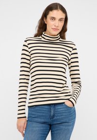 Haut à col roulé rayé noir et crème avec manches longues, en tissu à texture côtelée. Associé à un jean en denim bleu.