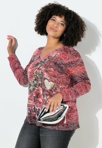Bluzka z długim rękawem i dekoltem w serek w czerwono-szarym wzorze z kwiatowymi i motylkowymi nadrukami. Połączona z metaliczną kopertówką i ciemnymi dżinsami.