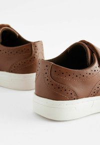 Zapatos de cuero marrón con diseño perforado, suelas de goma blanca y textura suave. Presentan una puntera redondeada y talón reforzado.
