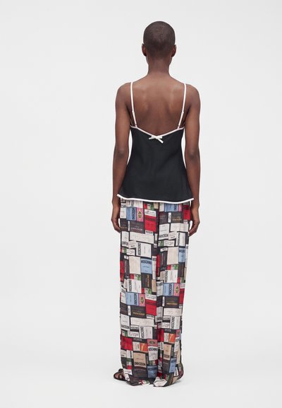 Personne vue de dos portant un caraco noir avec un liseré blanc et un pantalon à jambes larges couvert de motifs variés de textes et d'étiquettes.