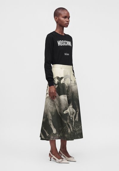 Personne portant un haut noir à manches longues avec le texte "Moschino Milano" et une jupe longue avec un imprimé mouton noir et blanc, avec des talons blancs.
