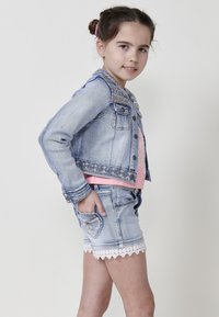 Denim jakna svetlega pranja, klasičnega kroja in srebrnimi detajli; v kompletu z usklajenimi kratkimi hlačami s čipkastim robom in žepi.