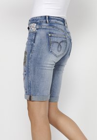Shorts en denim avec un tissu bleu clair, des ourlets roulés, des accents brodés de différentes couleurs et un détail de poche à motifs.