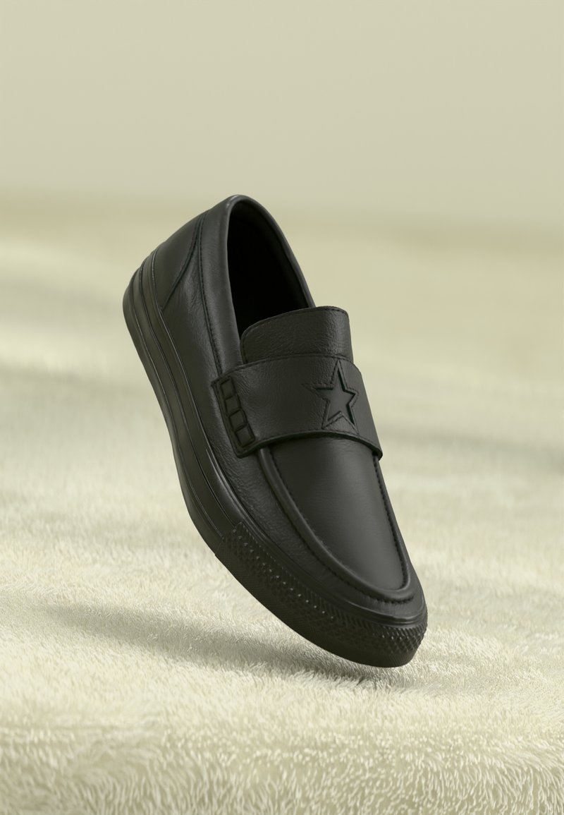 Sorte lær slip-on sko med flat såle, med en fremtredende stjerneaksent på stroppen og subtile sømdetaljer.