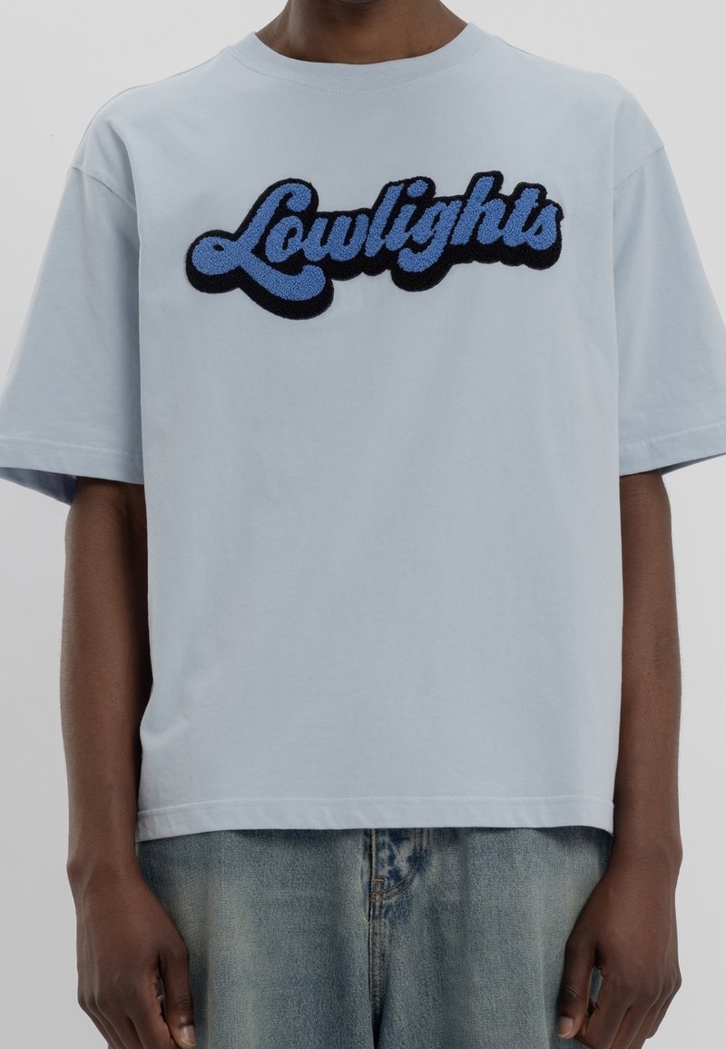 T-shirt bleu clair en coton doux avec un graphique texturé noir et bleu "Lowlights". Manches courtes et coupe décontractée.