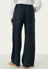 Navy wijde broek in lichte stof, met een zachte textuur, achterzakken en knopenaccenten. Gecombineerd met casual schoenen.
