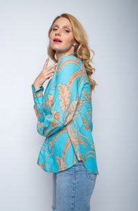 Turquoise shirt met een beige bloemenpatroon, lange mouwen, met knopen bij de manchetten en een relaxte pasvorm, gecombineerd met lichtblauwe spijkerbroeken.