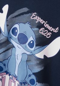 Camiseta de la Marina con un personaje de dibujos animados de pelaje azul claro y grandes ojos, texto que dice "Experimento 626," y degradados de colores en el fondo.