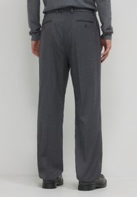 Pantalon gris sur mesure avec une finition texturée, dotés de deux poches arrière et d'une coupe droite. Porté avec des chaussures noires.