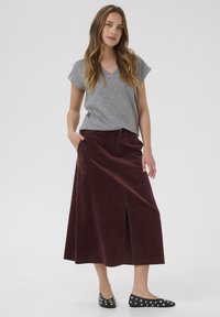 T-shirt grigio con scollo a V abbinato a una gonna midi in velluto a coste bordeaux con uno spacco frontale, completato da ballerine nere con accenti argentati.