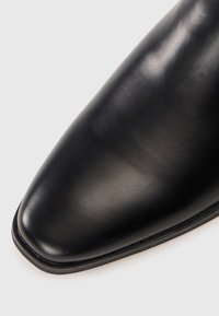 Zwarte leren dresschoen met een puntige neus, gladde textuur, minimale stiksels en een platte zool, gericht op een slanke, gepolijste uitstraling.
